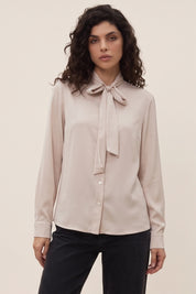 Front view of a woman wearing the beige Charming Blouse by FemeAdor with bowtie detail and flattering drape, ideal for professional and casual styling