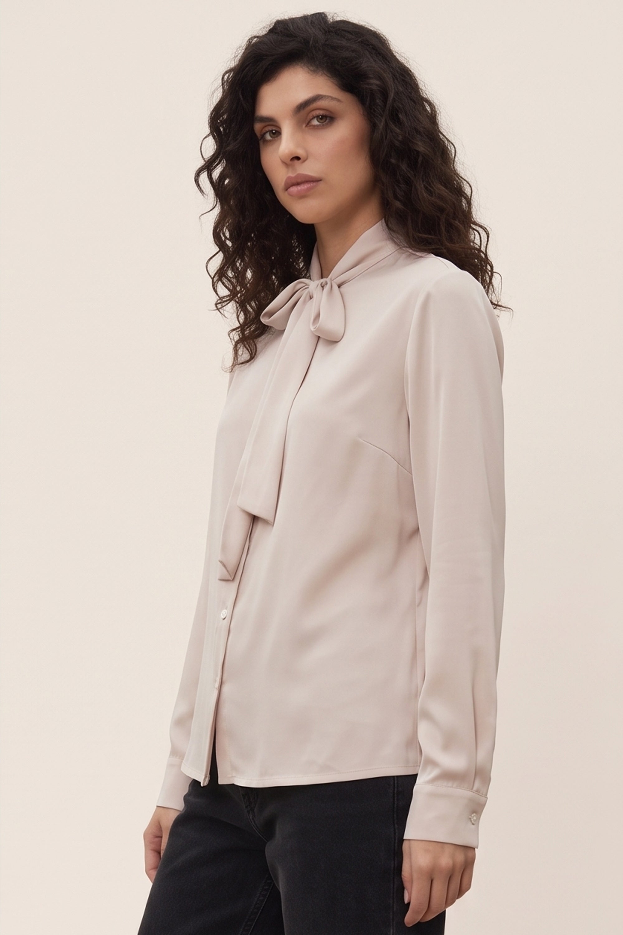 Side view of a woman wearing the beige Charming Blouse by FemeAdor with bowtie detail and flattering drape, ideal for professional and casual styling