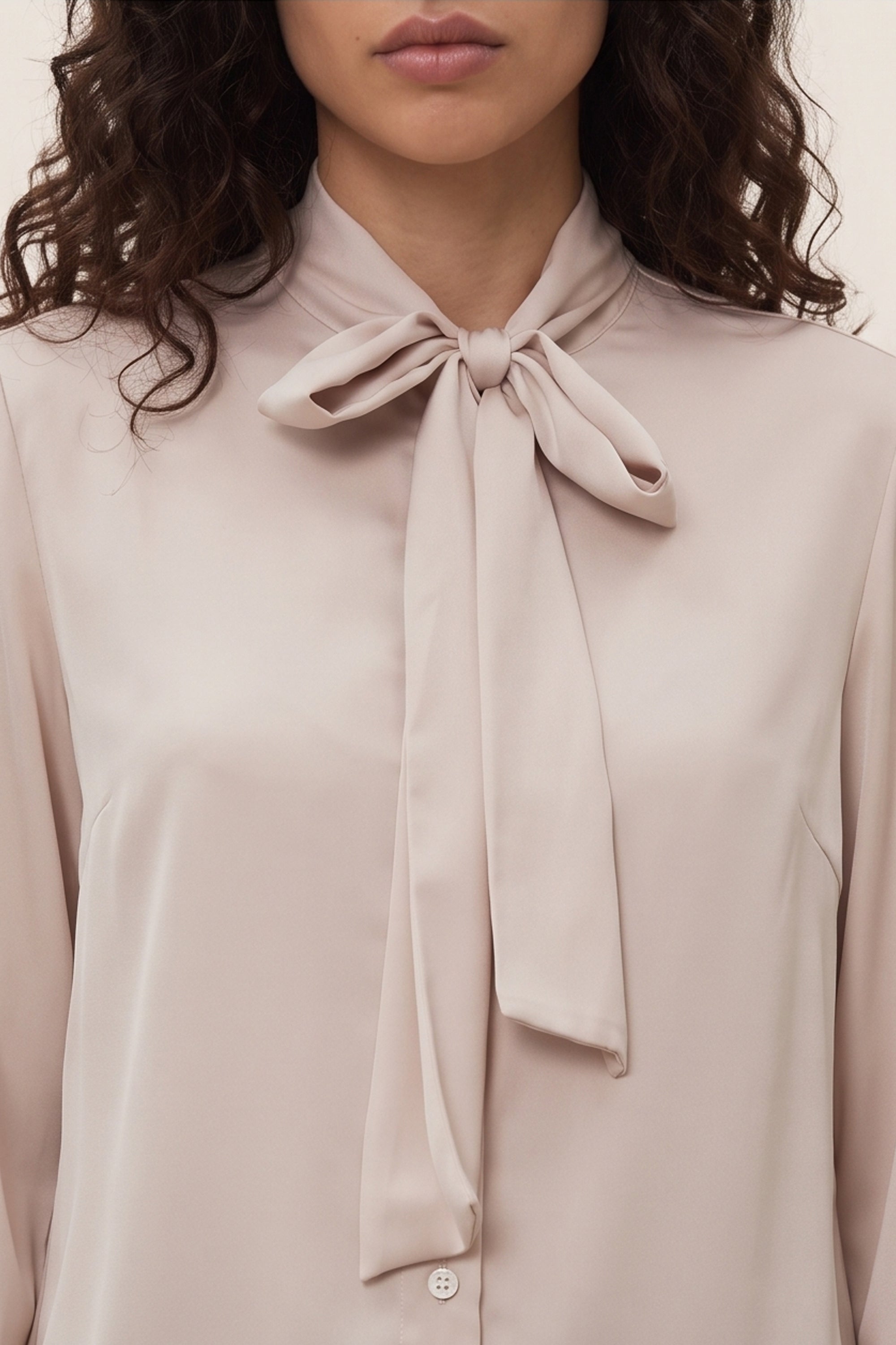 Close up view of a woman wearing the beige Charming Blouse by FemeAdor with bowtie detail and flattering drape, ideal for professional and casual styling