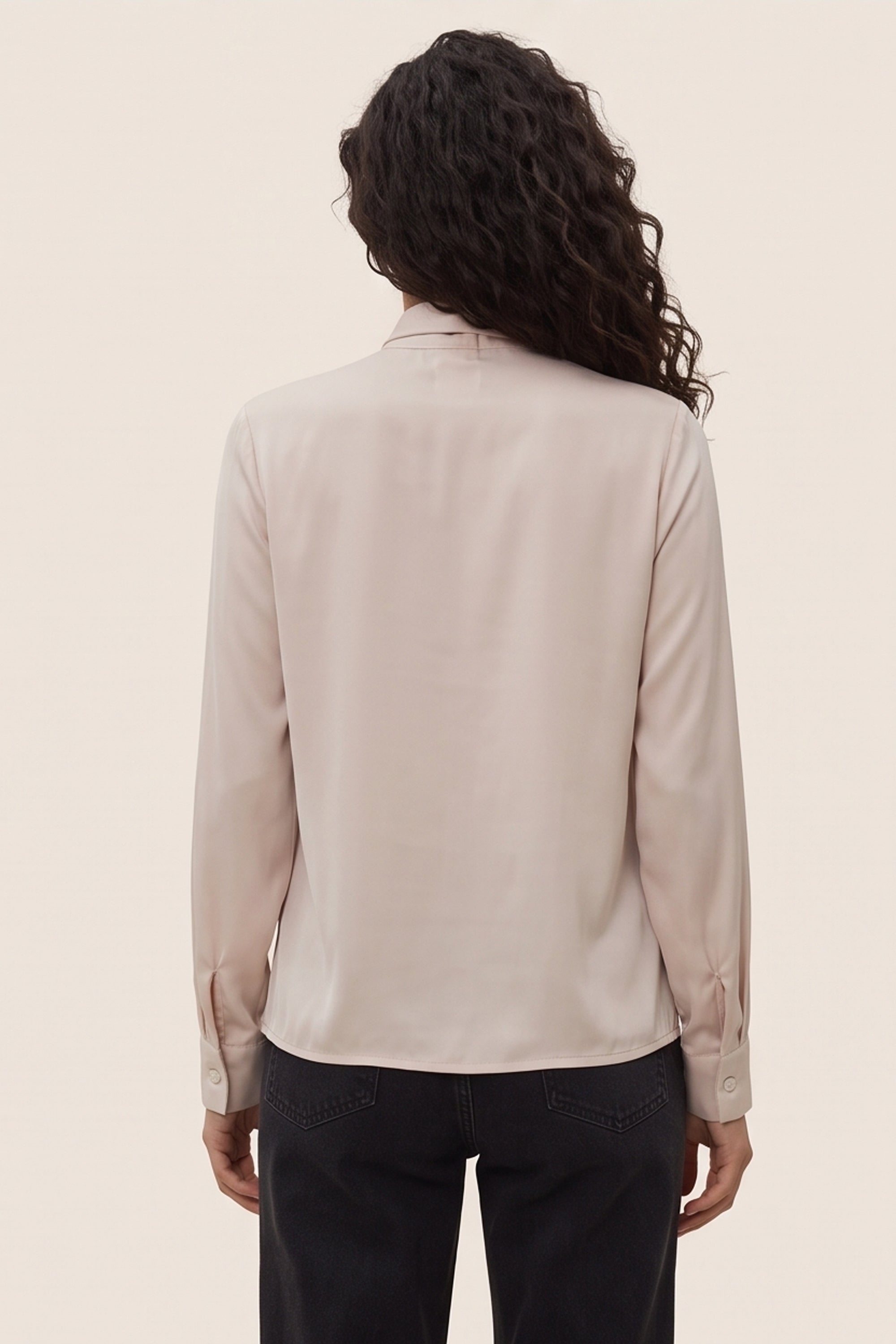 Back view of a woman wearing the beige Charming Blouse by FemeAdor with bowtie detail and flattering drape, ideal for professional and casual styling