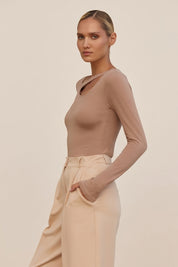 Side view of a woman wearing the beige Cut Longsleeve top by FemeAdor with fitted silhouette and front cutout detail