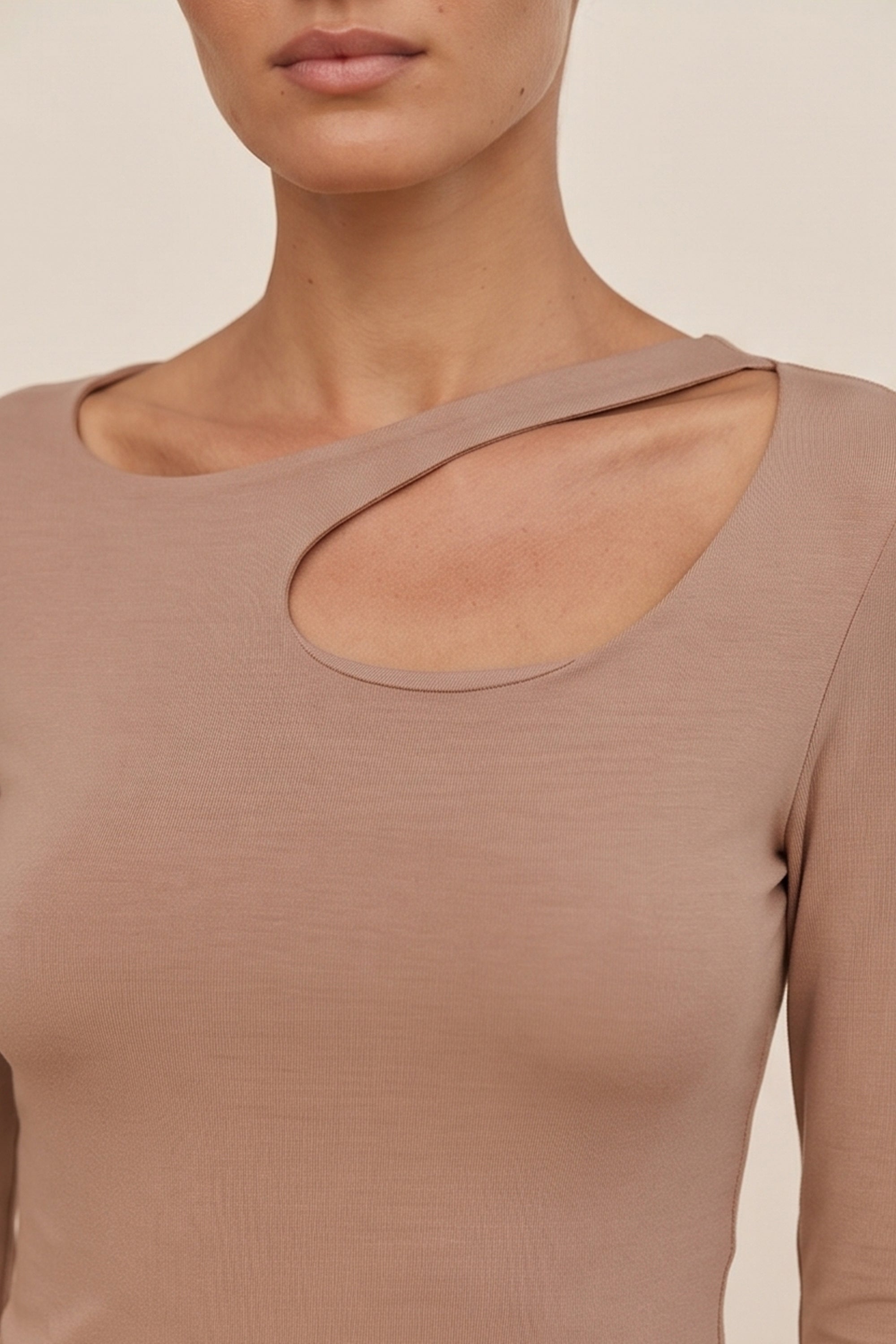 Close up view of a woman wearing the beige Cut Longsleeve top by FemeAdor with fitted silhouette and front cutout detail