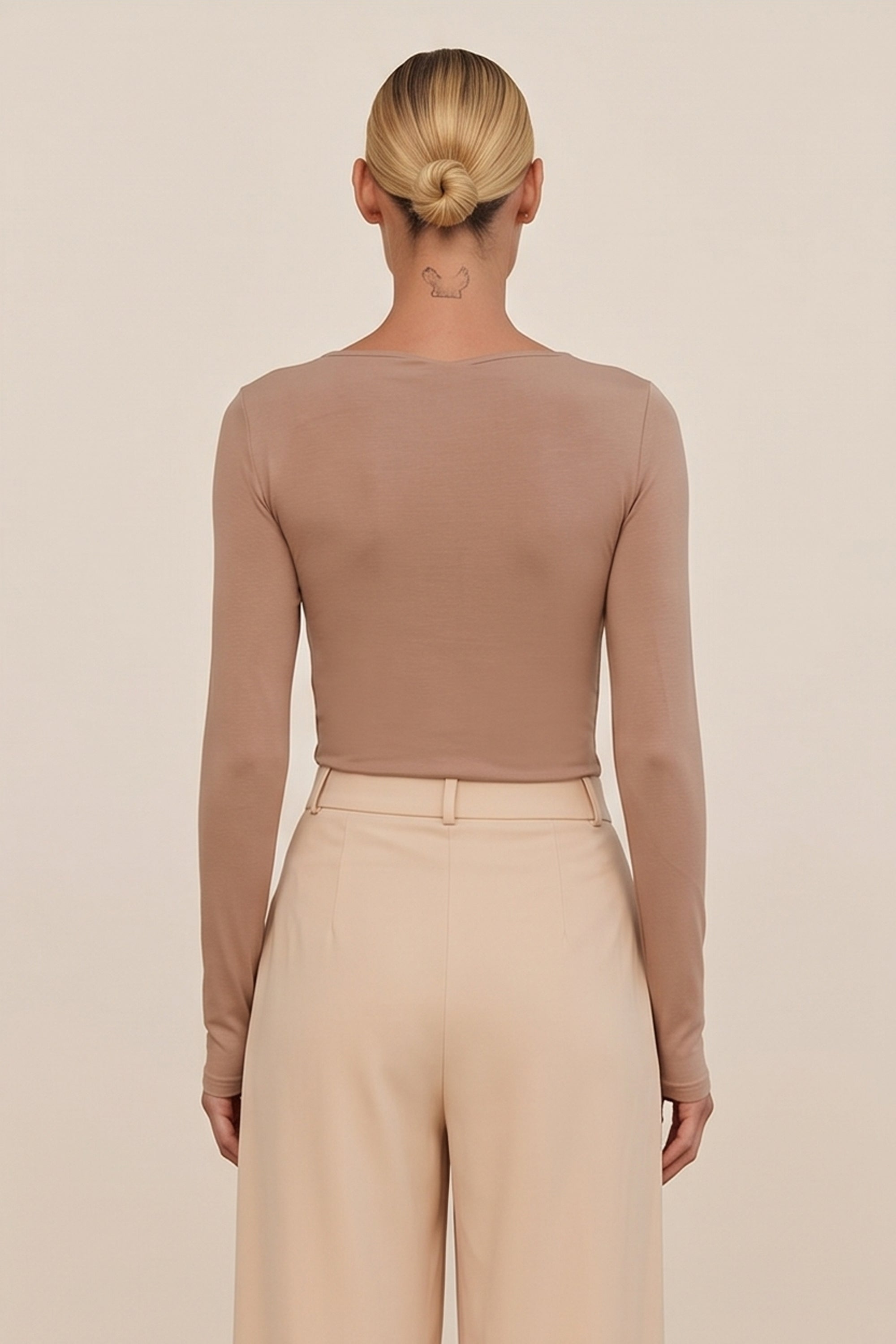 Back view of a woman wearing the beige Cut Longsleeve top by FemeAdor with fitted silhouette and front cutout detail