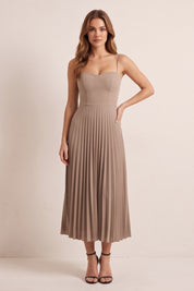 Front view of a woman wearing the beige Eclipse Demi Dress by FemeAdor featuring a structured corset top and a flowing pleated midi skirt perfect for formal and casual events