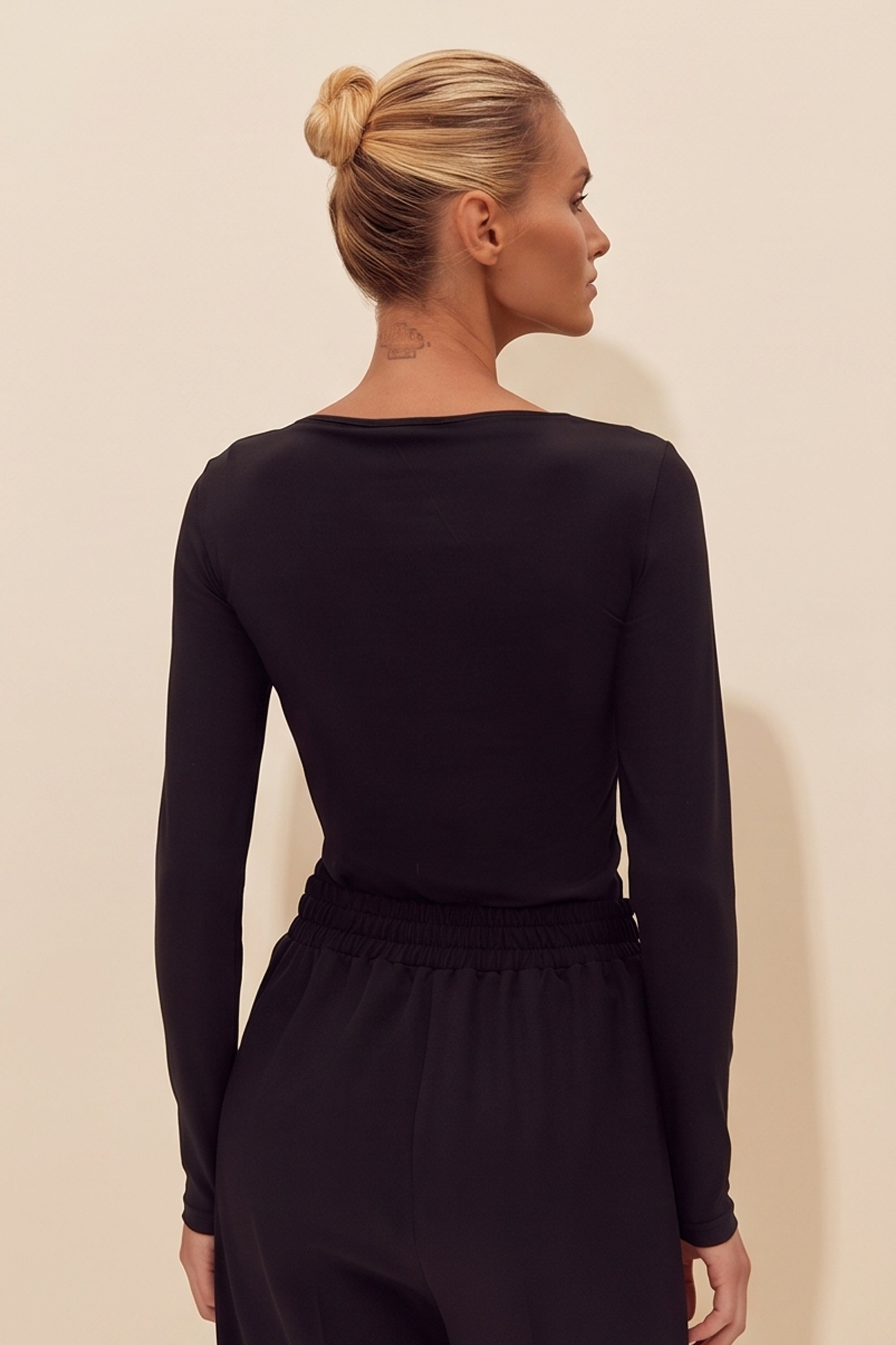 Back view of a woman wearing the black Cut Longsleeve top by FemeAdor with fitted silhouette and front cutout detail
