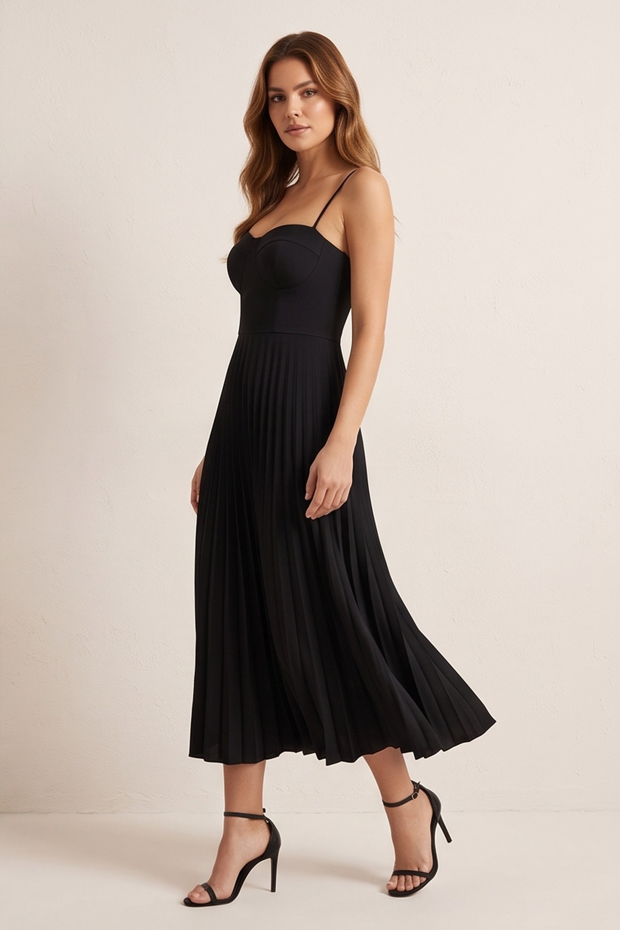 Side view of a woman wearing the black Eclipse Demi Dress by FemeAdor featuring a structured corset top and a flowing pleated midi skirt perfect for formal and casual events