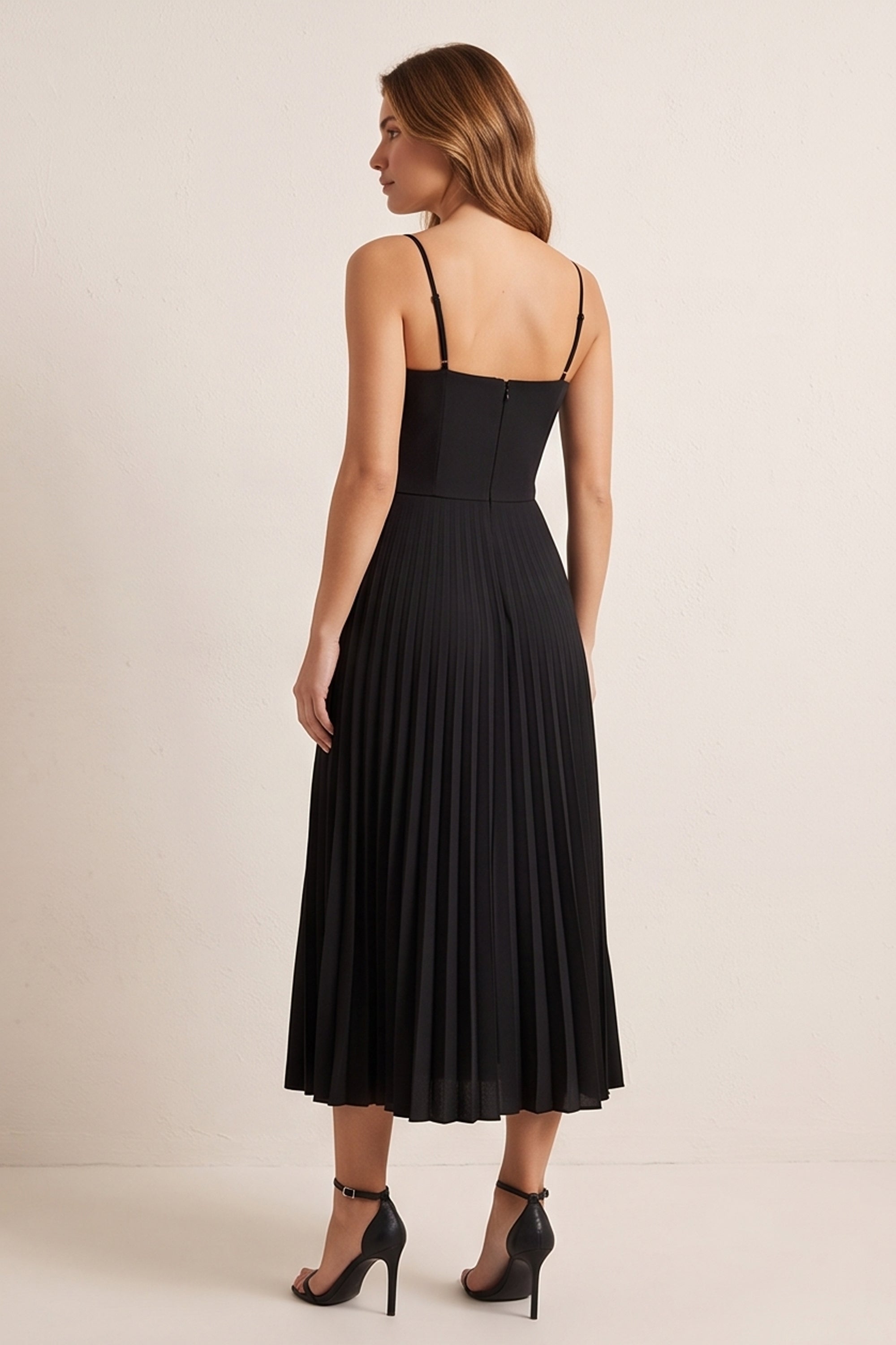 Back view of a woman wearing the black Eclipse Demi Dress by FemeAdor featuring a structured corset top and a flowing pleated midi skirt perfect for formal and casual events