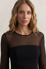 Close up view of a woman wearing the black noir midi dress by FemeAdor featuring a sheath silhouette and sheer front insert for an elegant, modern look