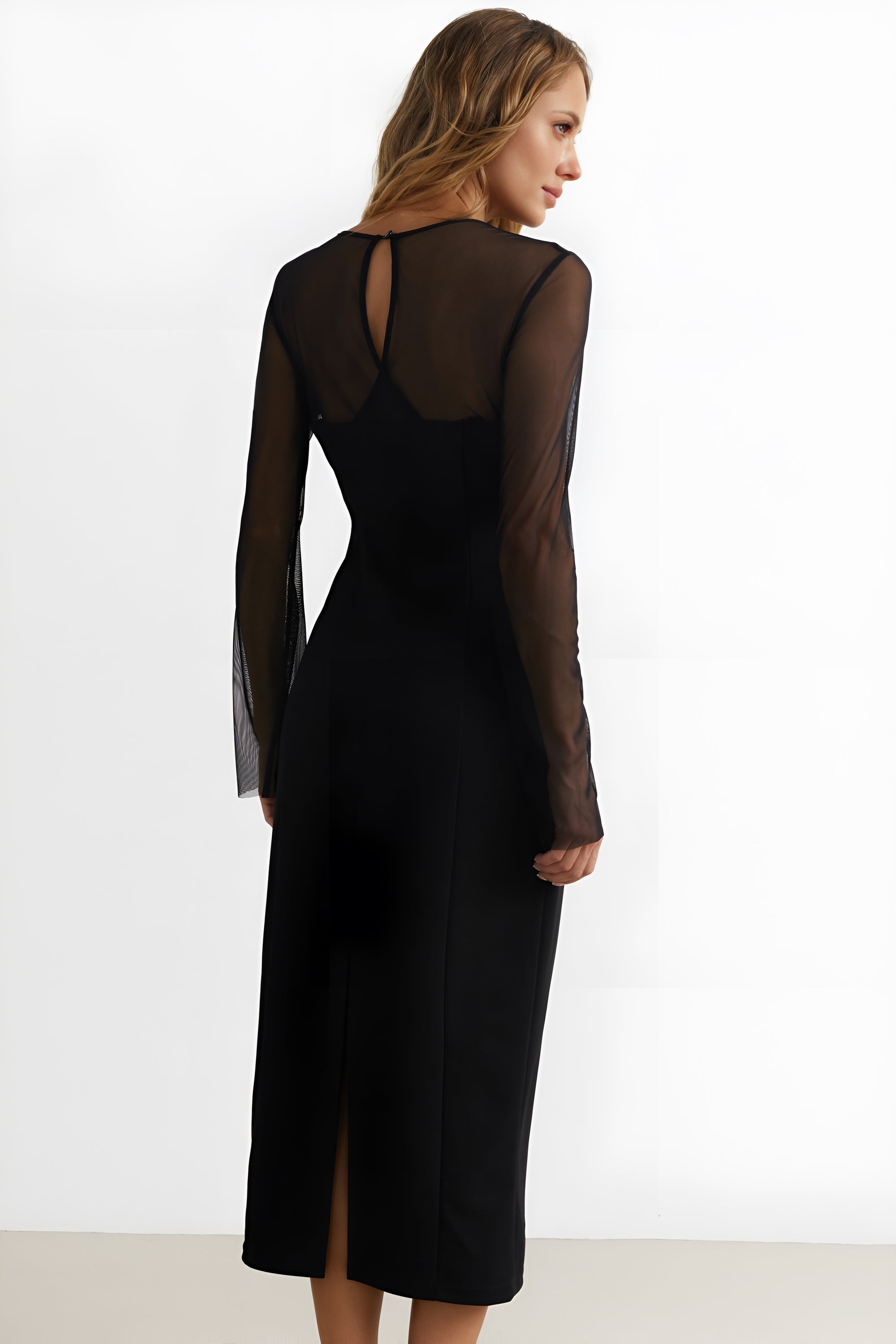 Back view of a woman wearing the black noir midi dress by FemeAdor featuring a sheath silhouette and sheer front insert for an elegant, modern look