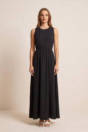 Front view of a woman wearing the black Virella Maxi Dress with sleeveless design, open back, and floor-length silhouette for elegant evening wear