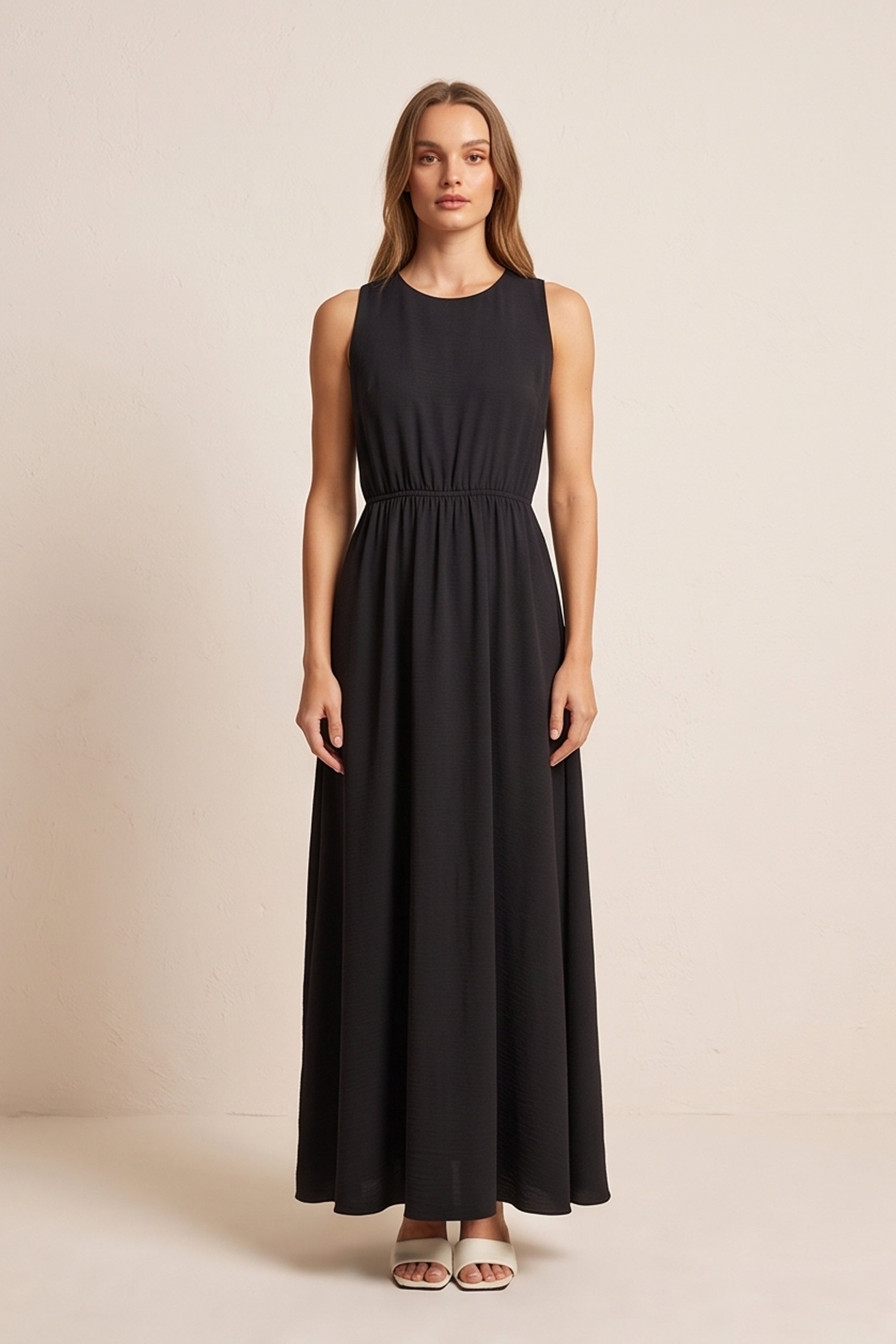 Front view of a woman wearing the black Virella Maxi Dress with sleeveless design, open back, and floor-length silhouette for elegant evening wear