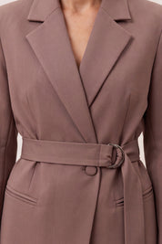 Close-up of a taupe-brown belted wrap coat with notched lapels and a silver-tone ring detail at the waist, shown on a model.