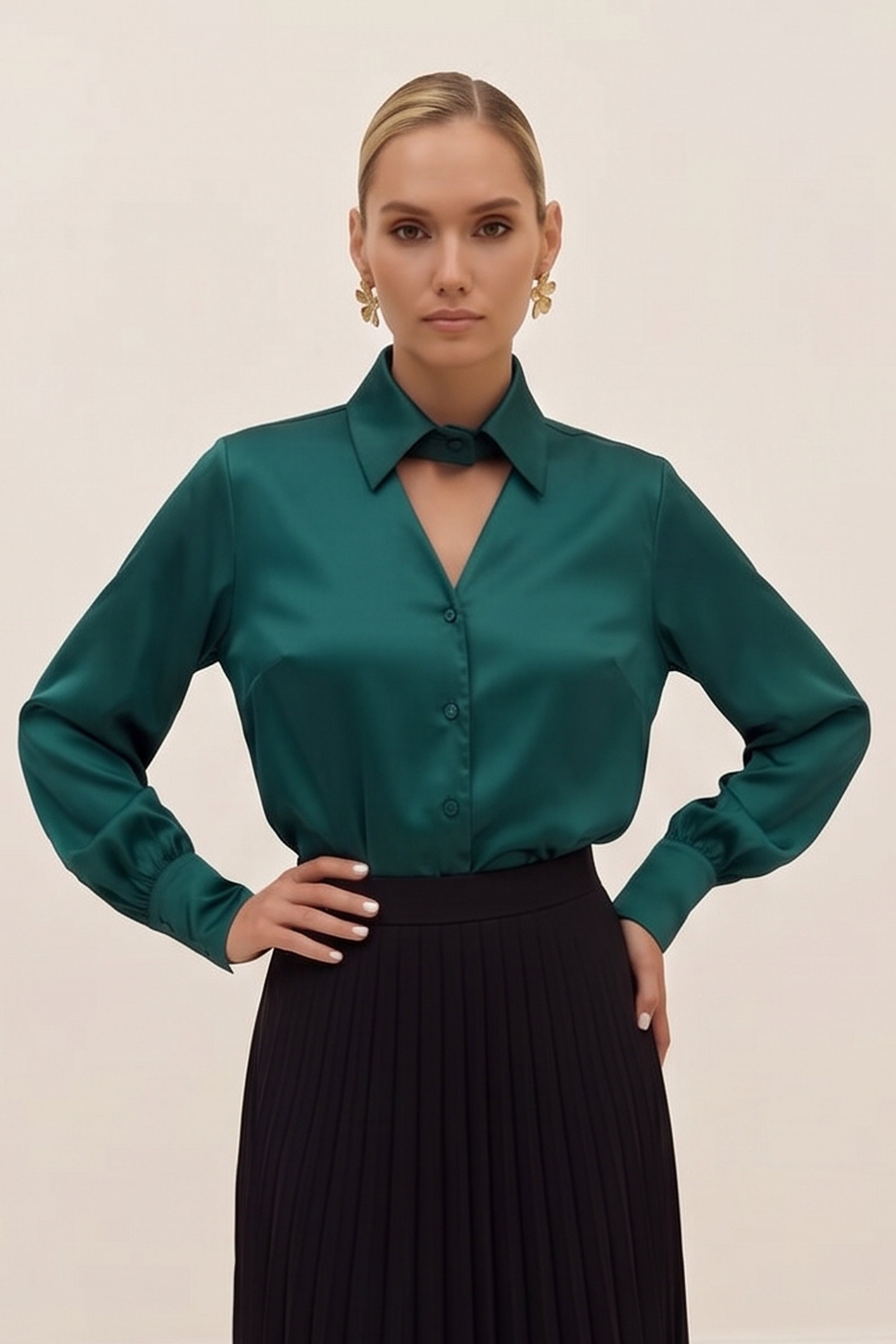 Front view of a woman wearing a silk like green eminence blouse by femeador and black skirt against a beige background