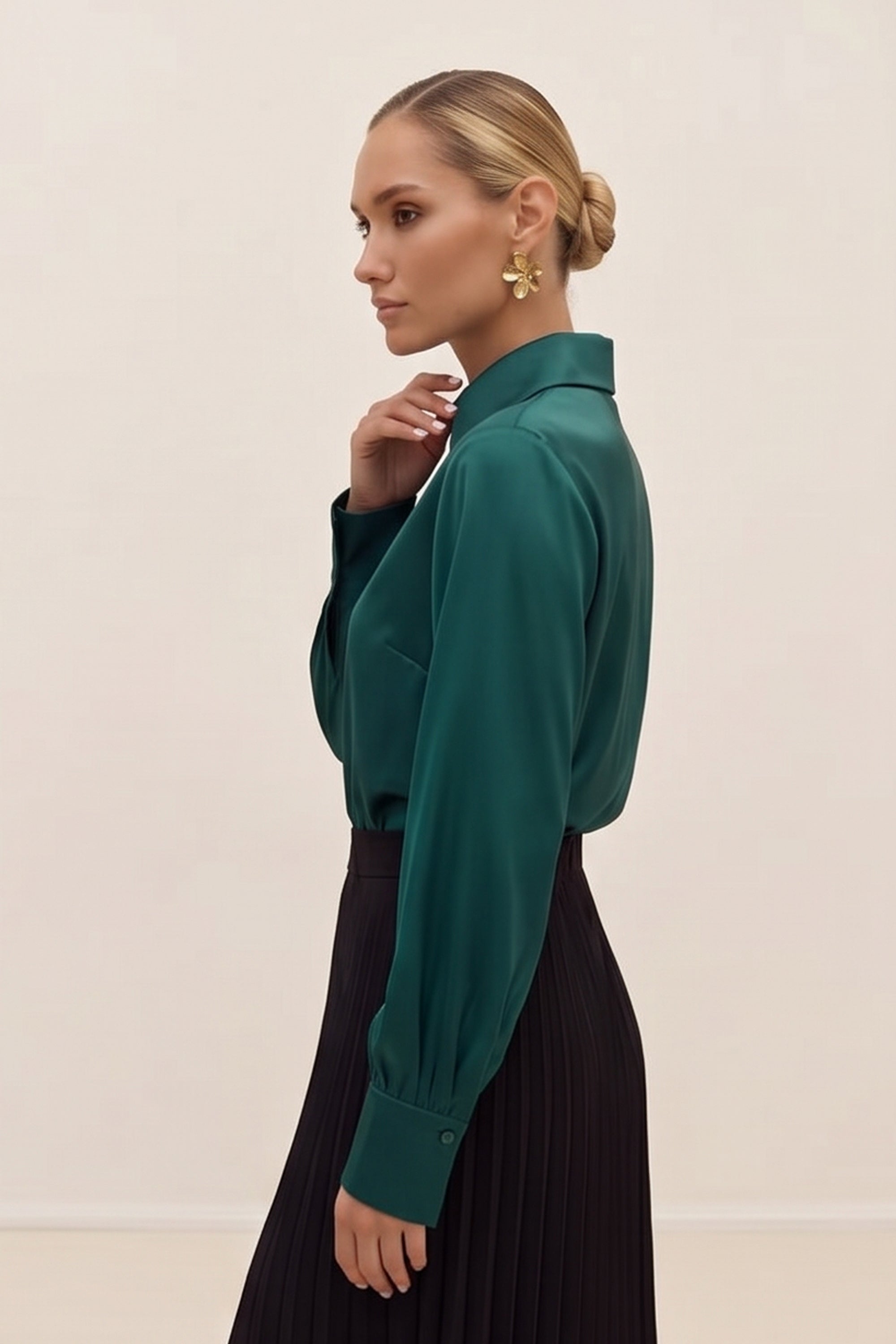 Side view of a woman wearing a silk like green eminence blouse by femeador and black skirt against a beige background