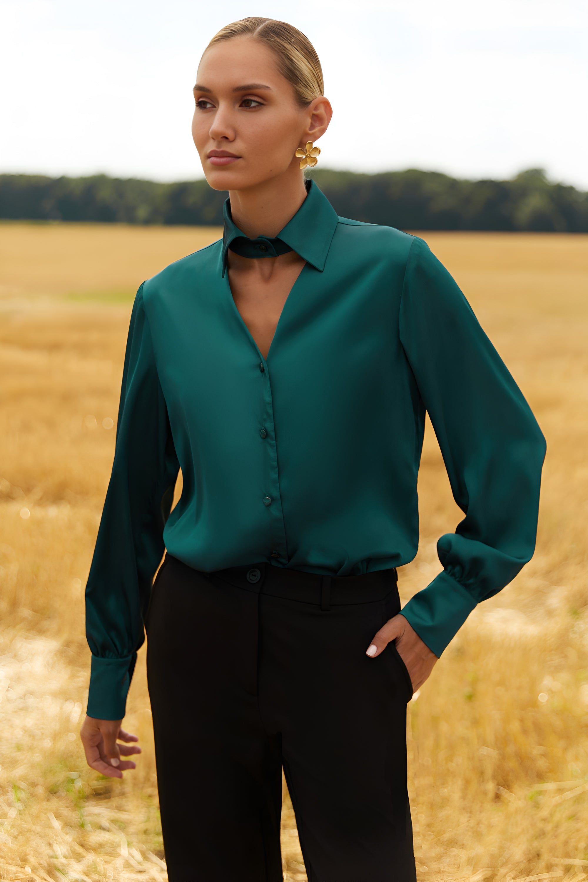 Front view of a woman wearing a green blouse and black pants standing in a field.