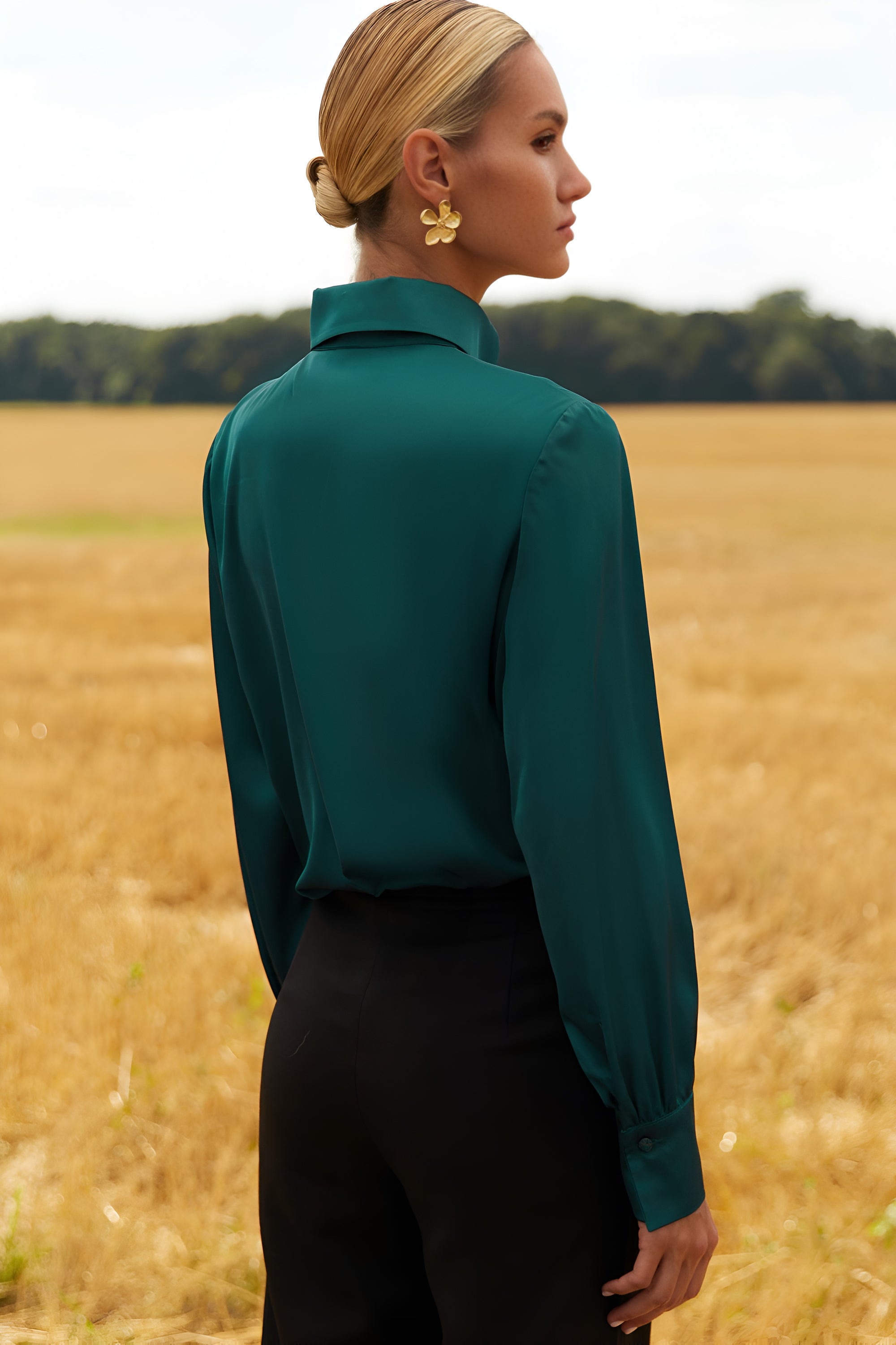 Back view of a woman wearing a green blouse and black pants standing in a field.