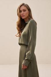 Side view of a woman wearing the green satin Nora Blouse with silk-like sheen and flattering drape, perfect for work or special occasions