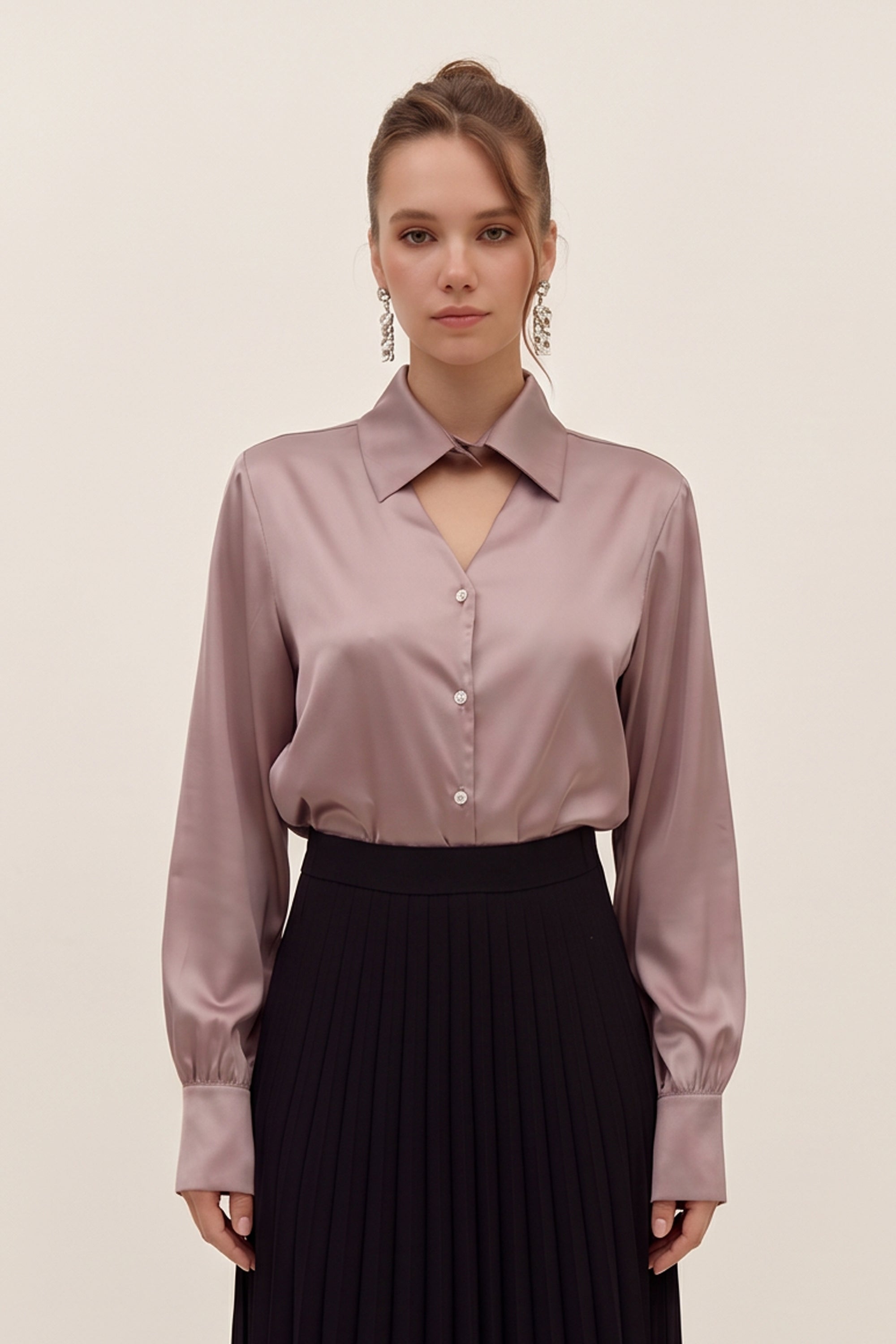 Front view of a woman wearing a light silk like pink eminence blouse by femeador and black skirt against a beige background