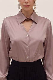 Close up view of a woman wearing a light silk like pink eminence blouse by femeador and black skirt against a beige background