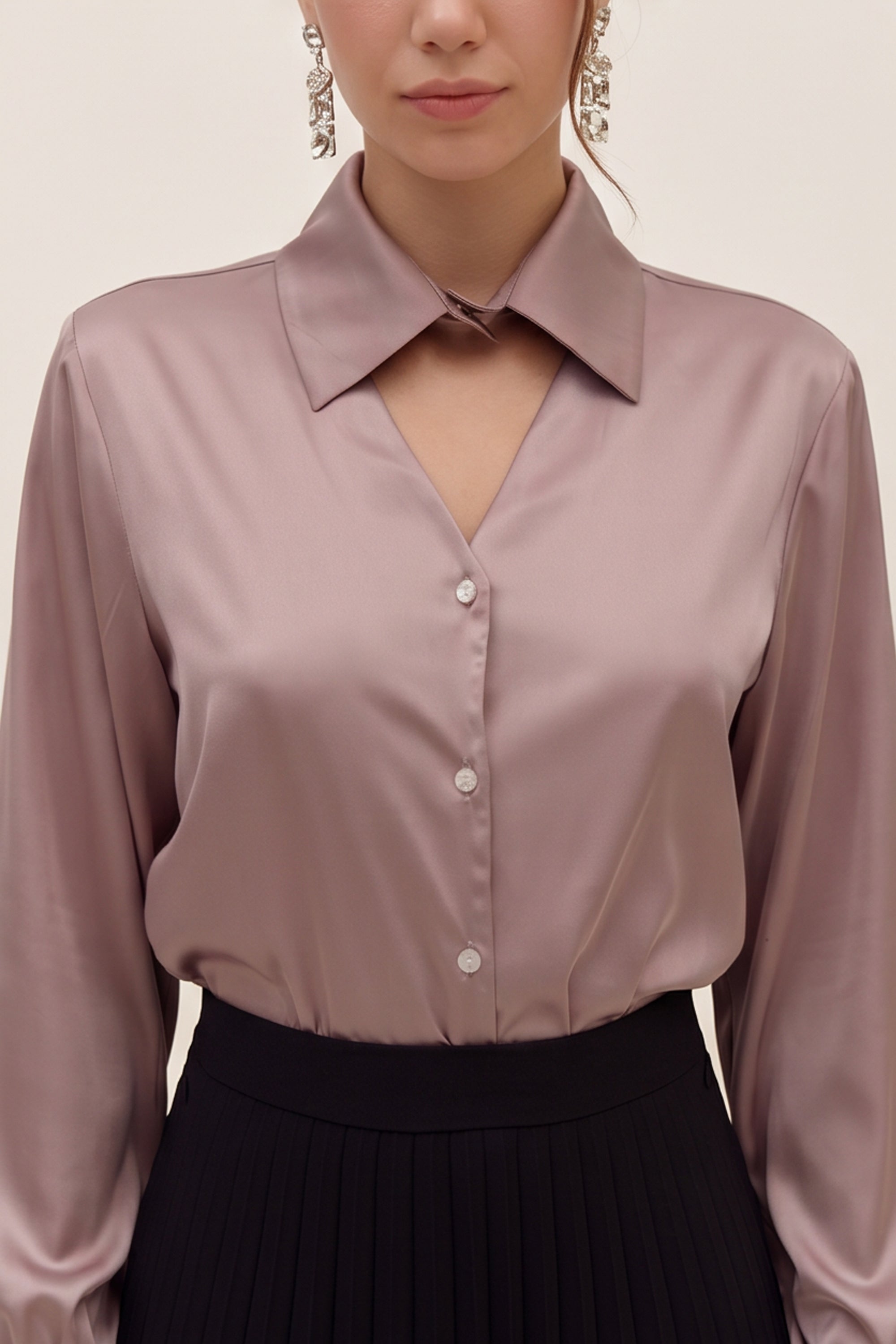 Close up view of a woman wearing a light silk like pink eminence blouse by femeador and black skirt against a beige background