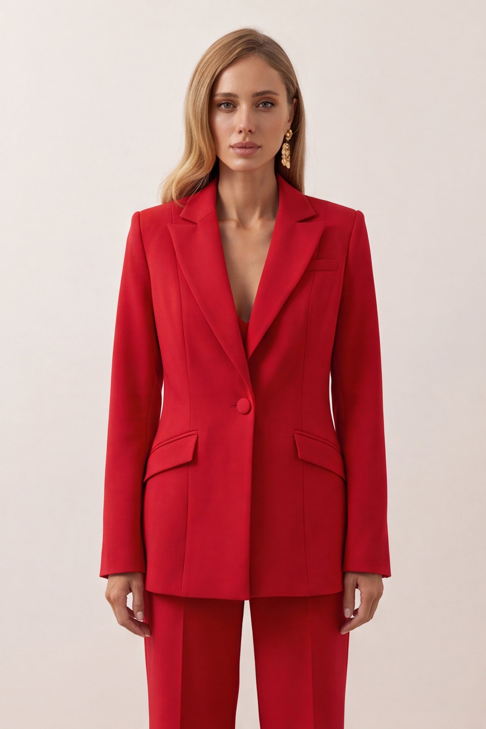 A woman shown from the front wearing a bright red tailored blazer and matching red trousers against a plain light beige studio background.