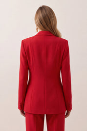 A woman shown from the back wearing a bright red tailored blazer and matching red trousers against a plain light beige studio background.