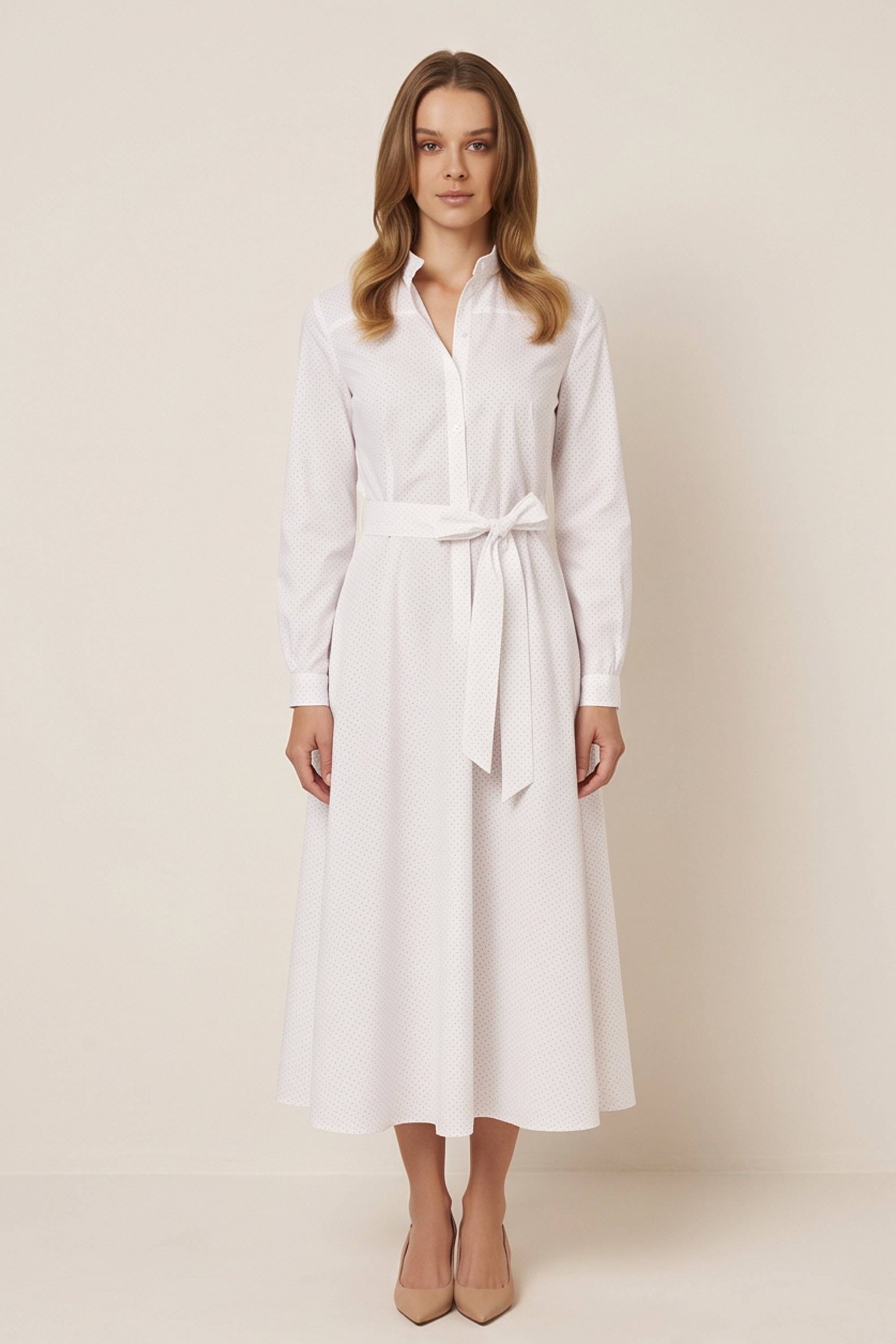 Front view of a woman wearing the white Liora Midi Dress by FemeAdor with polka dots, featuring a button-down front and flattering belted waistline