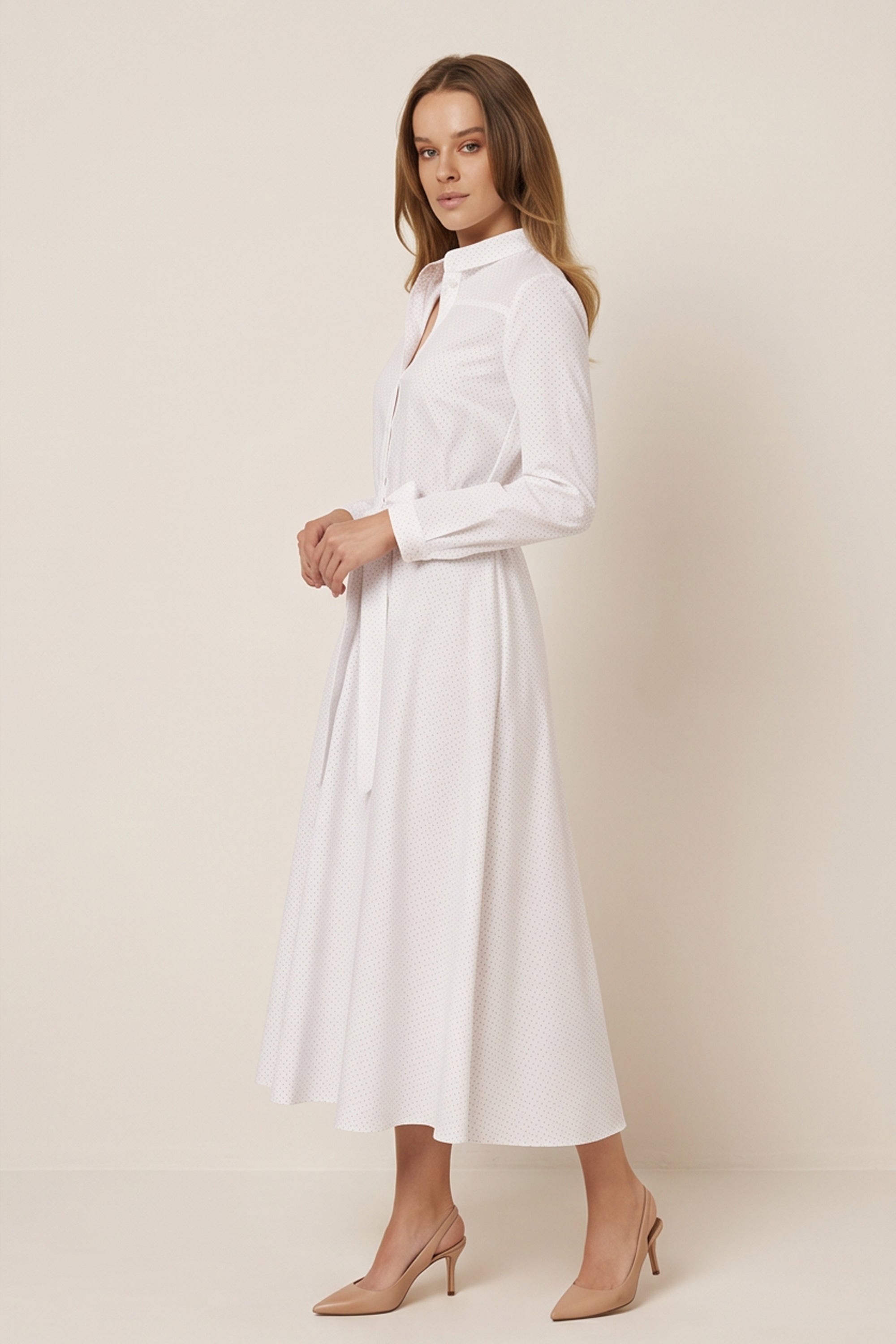 Side view of a woman wearing the white Liora Midi Dress by FemeAdor with polka dots, featuring a button-down front and flattering belted waistline