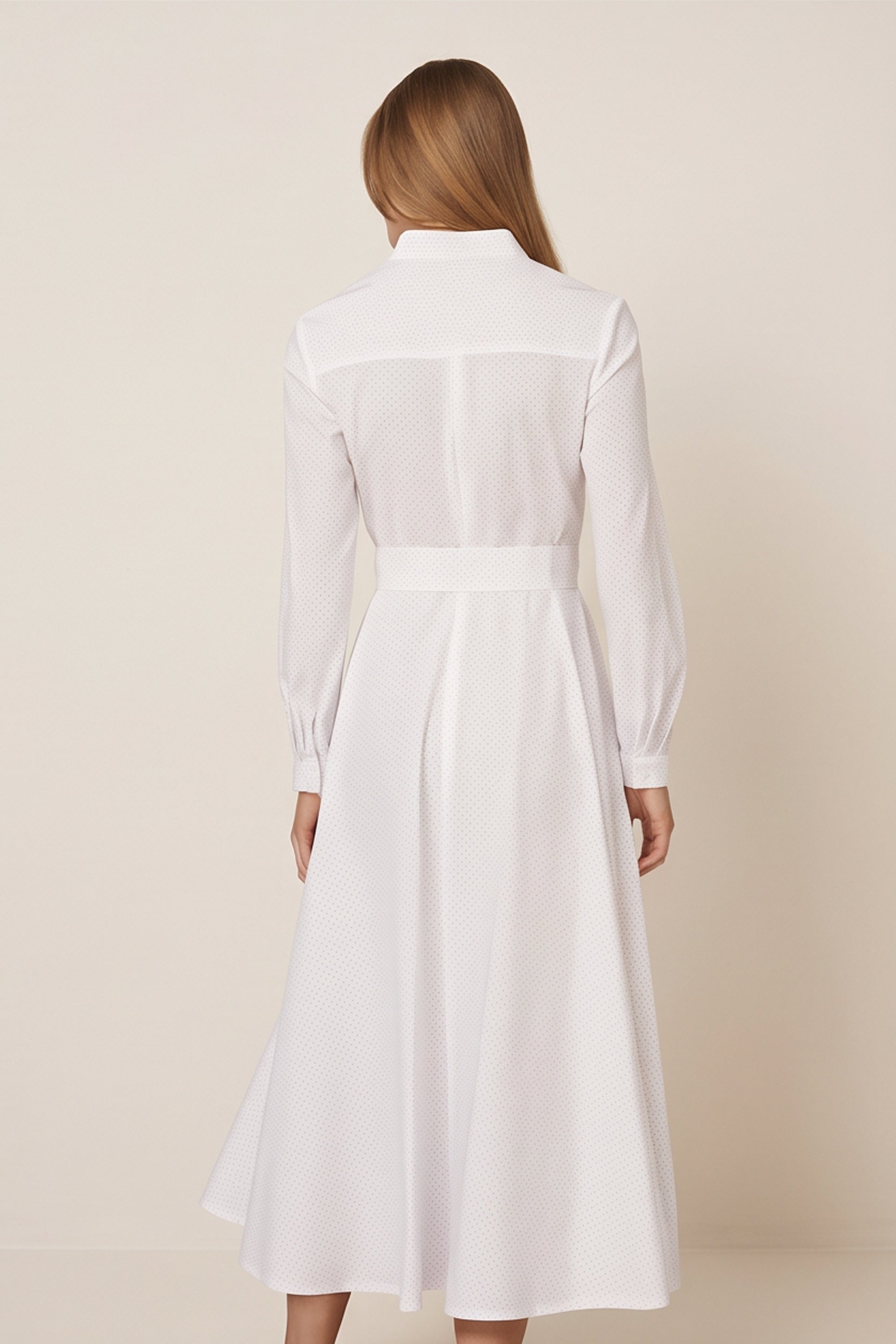 Back view of a woman wearing the white Liora Midi Dress by FemeAdor with polka dots, featuring a button-down front and flattering belted waistline