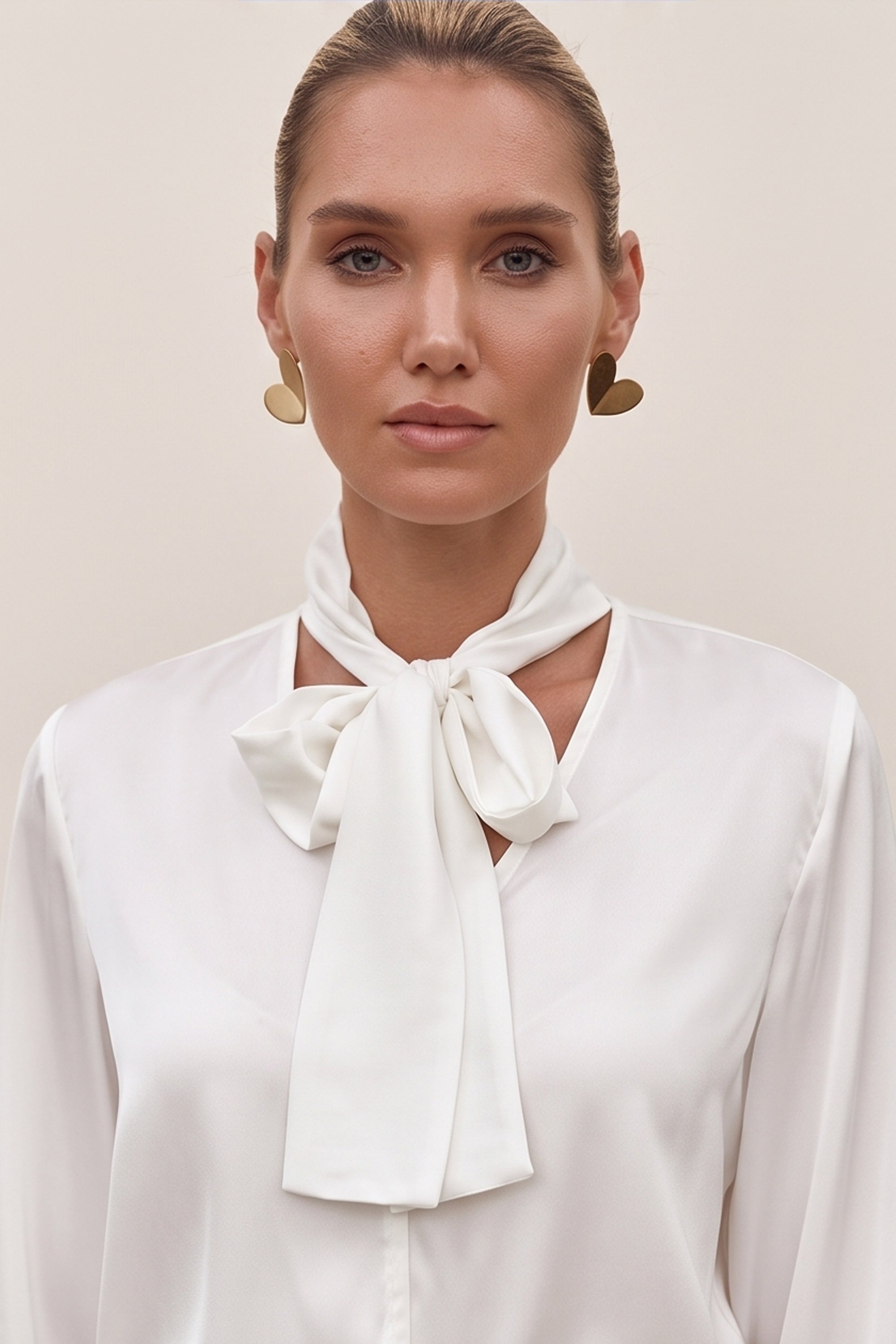 Close up view of a woman wearing a white reverie blouse by femeador with a bow tie and a blue pleated skirt on a beige background
