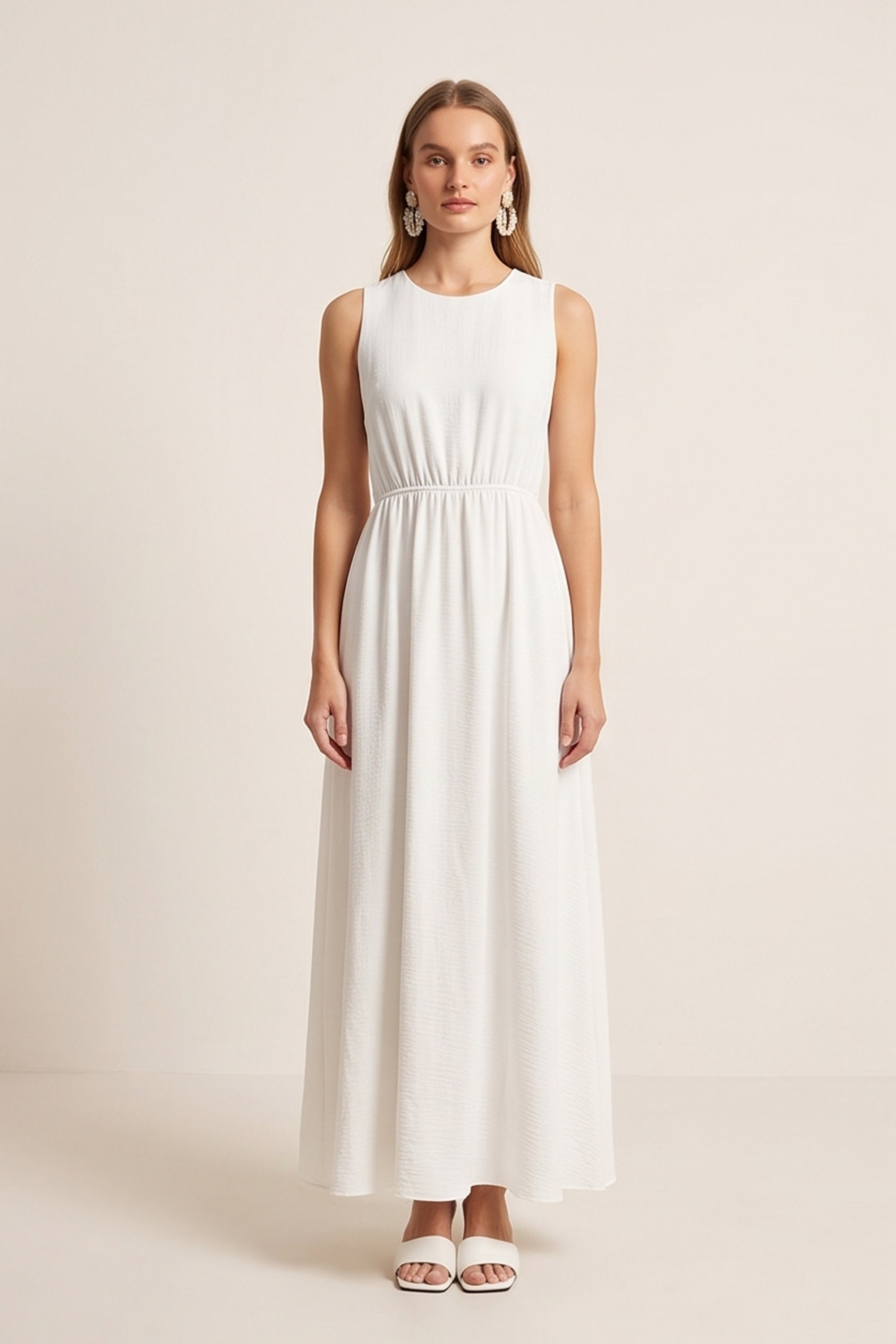 Front view of a woman wearing the white Virella Maxi Dress with sleeveless design, open back, and floor-length silhouette for elegant evening wear